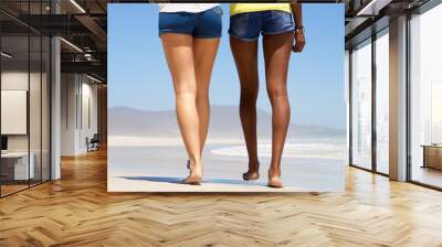 Rear view two women walking barefoot on beach Wall mural