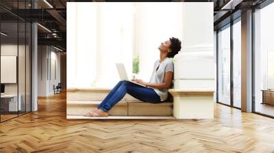 Relaxed young african woman sitting outside with her laptop Wall mural