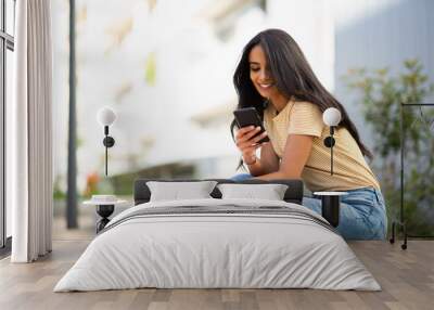 Side of young smiling woman sitting outside looking at mobile phone Wall mural