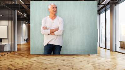 smiling older man leaning against wall with arms crossed and looking away Wall mural