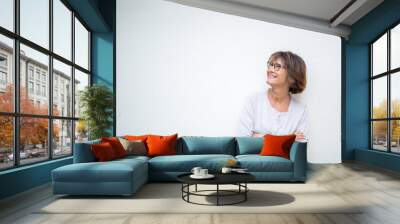 smiling older woman with arms crossed by white background looking away Wall mural