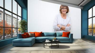 smiling older woman with arms crossed by white background Wall mural