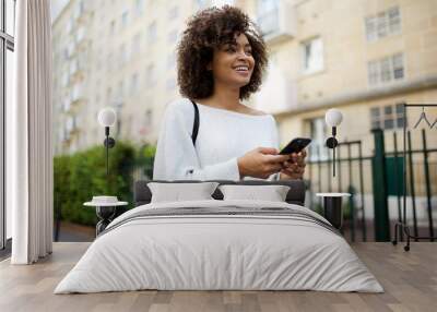 smiling young african american woman walking in city with mobile phone in hand Wall mural