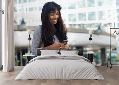 smiling young woman in the city with bag and looking at cellphone Wall mural