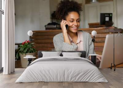 Smiling young woman using laptop and talking on mobile phone Wall mural