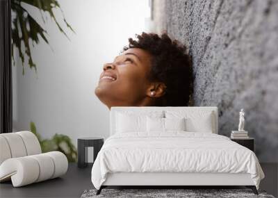 Young african woman leaning to a wall outside and looking up Wall mural