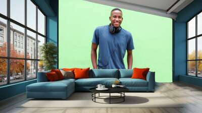 Young  man smiling with headphones against green background Wall mural