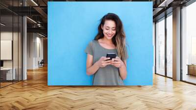 young smiling woman using mobile phone against blue background Wall mural