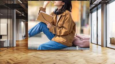 young thinking woman sitting outside with book Wall mural