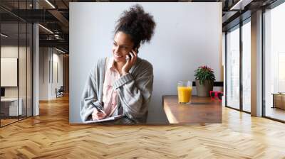 Young woman talking on mobile phone and taking notes Wall mural