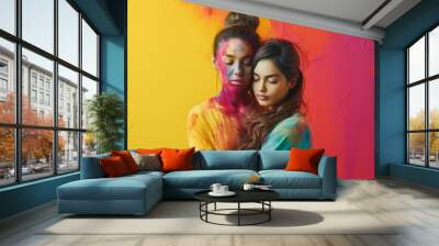 Two young girls embrace each other, covered in splashes of vibrant color, surrounded by a vivid, colorful background. This portrait symbolizes the union of love and artistic expression. Wall mural