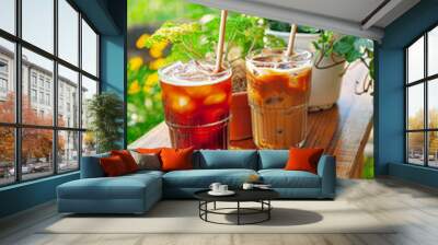 Ice tea and coffee is next to a potted plant on wooden table outdoors with garden backgound in sunny afternoon Wall mural