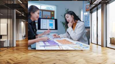 Two female ui/ux designers are working together in the office, discussing over a new mobile application interface wireframe design Wall mural