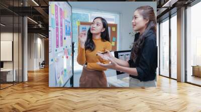 Two talented asian ui/ux designers collaborate on a mobile app wireframe in a dynamic office setting, embodying teamwork and creativity in a startup environment Wall mural