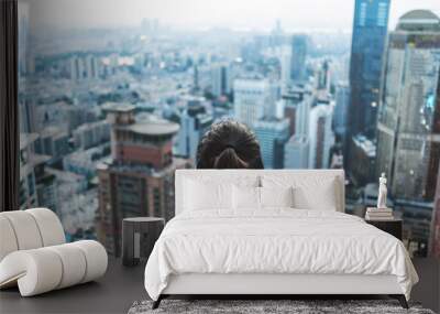 Young woman looks out over the city at the top of the building Wall mural