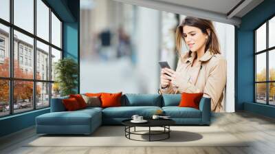 beautiful young woman standing at the street and using her mobile phone Wall mural