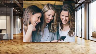 Three young woman sitting at cafe drinking coffee and looking at mobile phone
 Wall mural