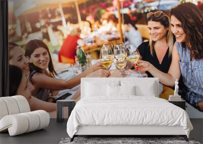 Young female friends clinking glasses with wine on the summer terrace of cafe or restaurant Wall mural