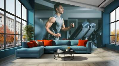 young man in sportswear running on treadmill at gym Wall mural