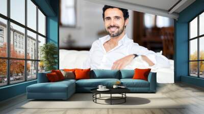 Happy smiling man relaxing and sitting on sofa at home Wall mural