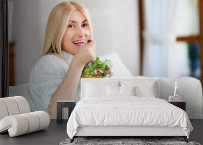 Mature woman eating a healthy salad on her sofa Wall mural