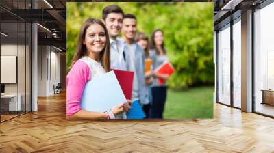 Outdoor portrait of a smiling young student in front of a group of students Wall mural