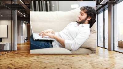 Portrait of a relaxed young guy using laptop at home Wall mural