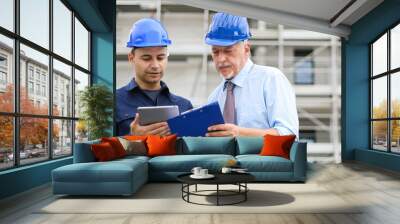 Two architect developers reviewing building plans at construction site using a tablet Wall mural