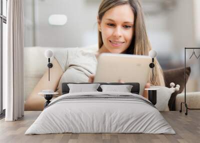 Young woman using a tablet on sofa at home Wall mural