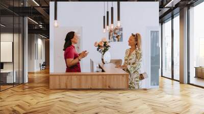 A beautiful blonde woman conversing with the dental clinic receptionist, scheduling an appointment for dental treatment with a bright smile Wall mural