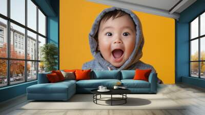 Close-up portrait of a surprised Asian toddler baby with open mouth in a casual hoodie on an isolated yellow background. for advertising background, banner or flyer with copy space for add text Wall mural