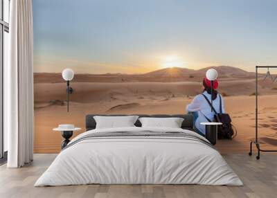 A young fermale traveler enjoys a sunrise or sunset landscape view of the desert sand dunes of Erg Chebbi near the village of Merzouga, Morocco. Wall mural