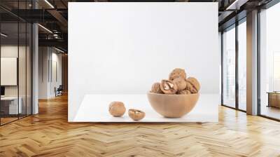 A wooden bowl with unpeeled walnuts stands on a white table. Wall mural