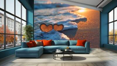 Two heart-shaped shells sit on the sandy beach, gently kissed by the waves as the sun sets in a warm, romantic glow. Wall mural