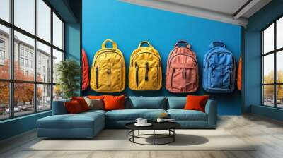 Colorful backpacks displayed against a blue wall in a new school setting Wall mural