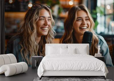 Two women enjoying a lively podcast session with laughter and joy in a cozy, well-lit setting. The image captures a moment of friendship and creativity. Wall mural