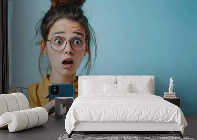 Unexpected Message: A young woman in glasses expresses shock and disbelief while looking at her phone Wall mural