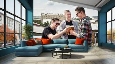 Happy smiling male friends drinking beer and clinking glasses at bar or pub on rooftop, copy space. Friendship and celebration concept Wall mural