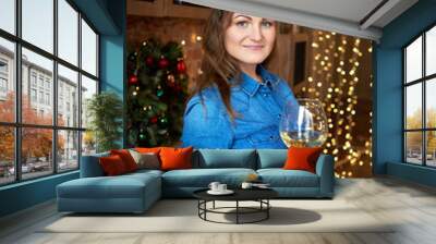 Happy smiling woman holding glass of wine in kitchen at home with Christmas decor and garland on background, copy space Wall mural