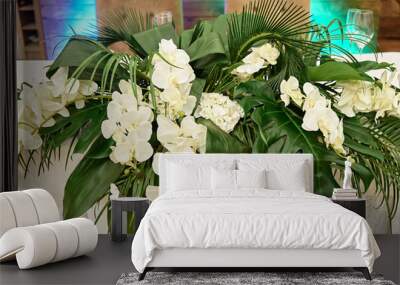 Lush floral arrangement of orchids and monstera leaves on wedding table. Wedding presidium in restaurant, copy space. Banquet table for newlyweds. Luxury wedding decor Wall mural