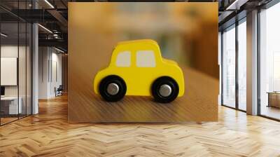 Closeup shot of a yellow wooden toy car on a wooden surface Wall mural