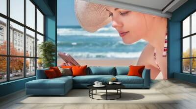 Beautiful woman in hat using her mobile phone on beach Wall mural