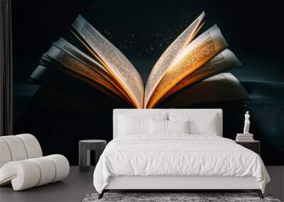 An open book with light shining from its pages, creating a mystical atmosphere in a darkened room Wall mural