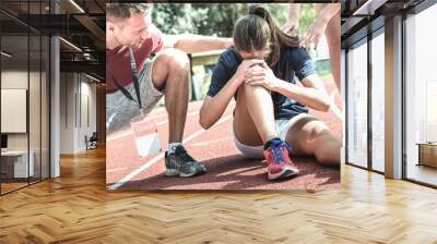 female athlete getting injured during athletic run training - male coach taking care on sport pupil  Wall mural