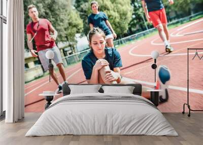 Female sportler getting injured at athletic workout training - Male coach taking care on sport pupil after physical accident - Team concept with young sporty people facing bad mishaps casualty Wall mural