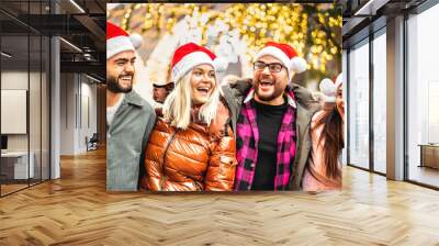 Happy friends group walking at city under Christmas tree decorations - Winter life style concept with young people wearing red santa claus hats having fun holiday together outside - Warm bright filter Wall mural