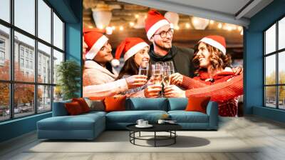 Young friends with santa hats celebrating Christmas with champagne wine toast at home reunion - Winter holidays concept with happy millenials enjoying time and having fun together - Focus on glasses Wall mural