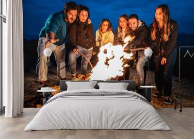 Young people having fun together at night party around bonfire - Wanderlust life style concept with happy friends traveler making themselves warm by campfire on dusk time - Vivid contrast filter Wall mural