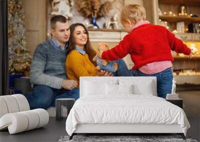 Little girl gives parents her toy. In the background new year tree Wall mural