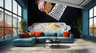 Female chef hands rub cheese on an old grater into baking dish. Ingredients for cooking of potato baked pudding with meat. Close up. Selective focus. Wall mural